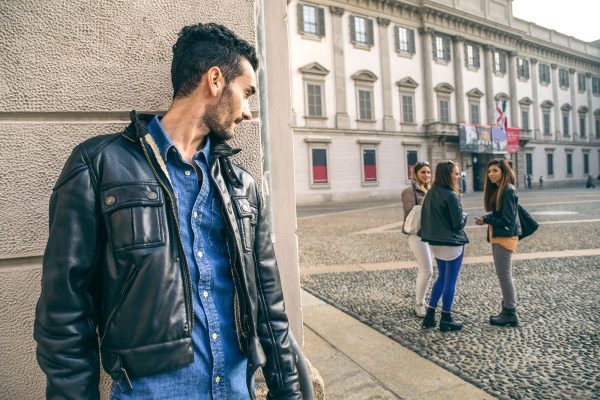 Un uomo appoggiato a un muro osserva tre donne in una piazza urbana.