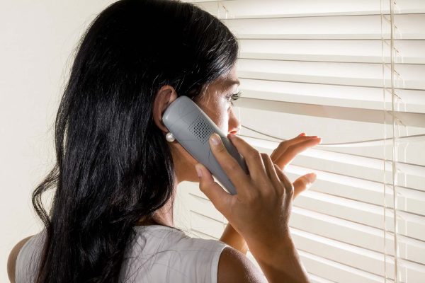Donna al telefono mentre guarda attraverso le persiane.